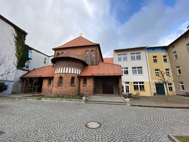 Backsteinkirche mit rotem Ziegeldach und gepflastertem Hof.