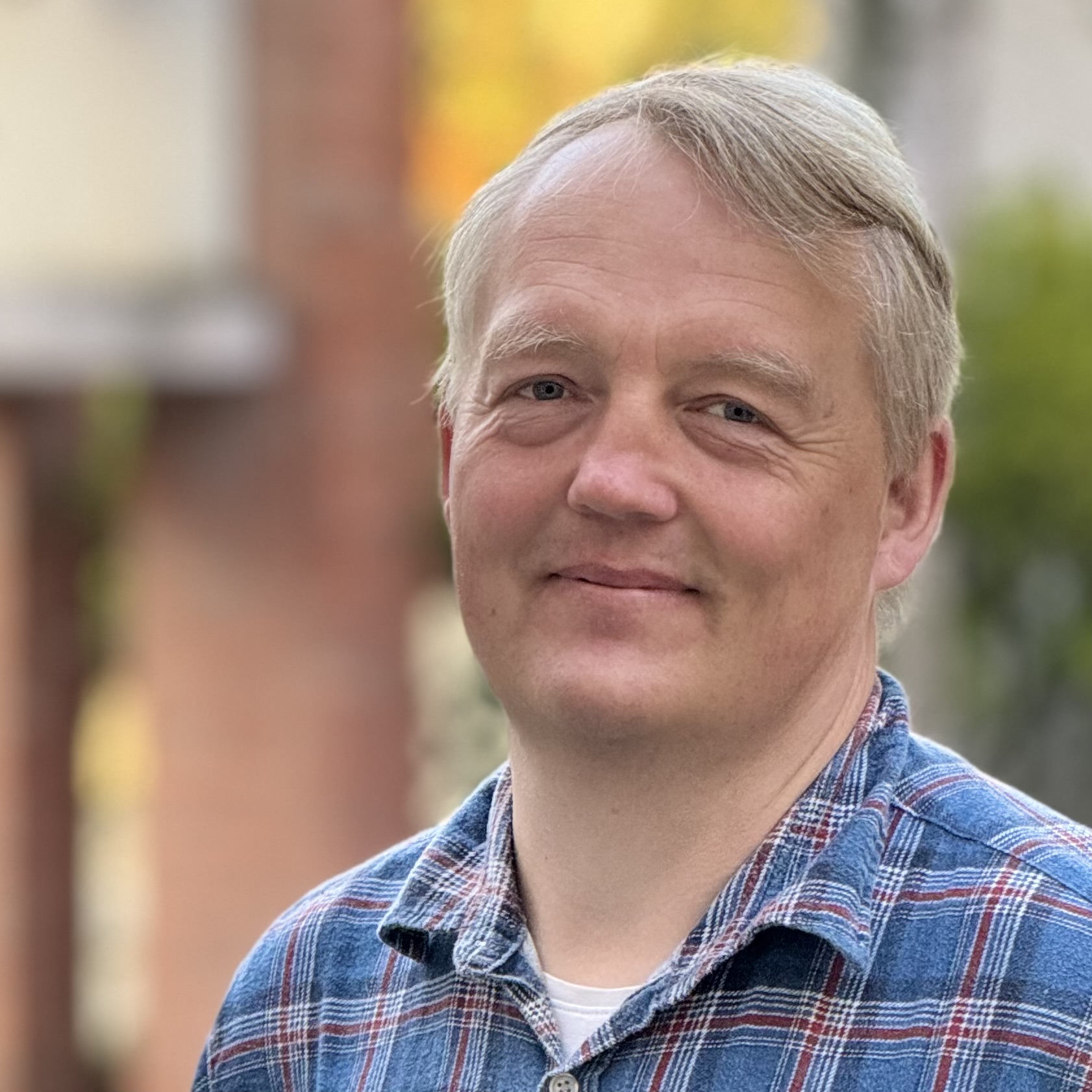 Porträt eines Mannes mit hellem Haar und einem karierten Hemd.