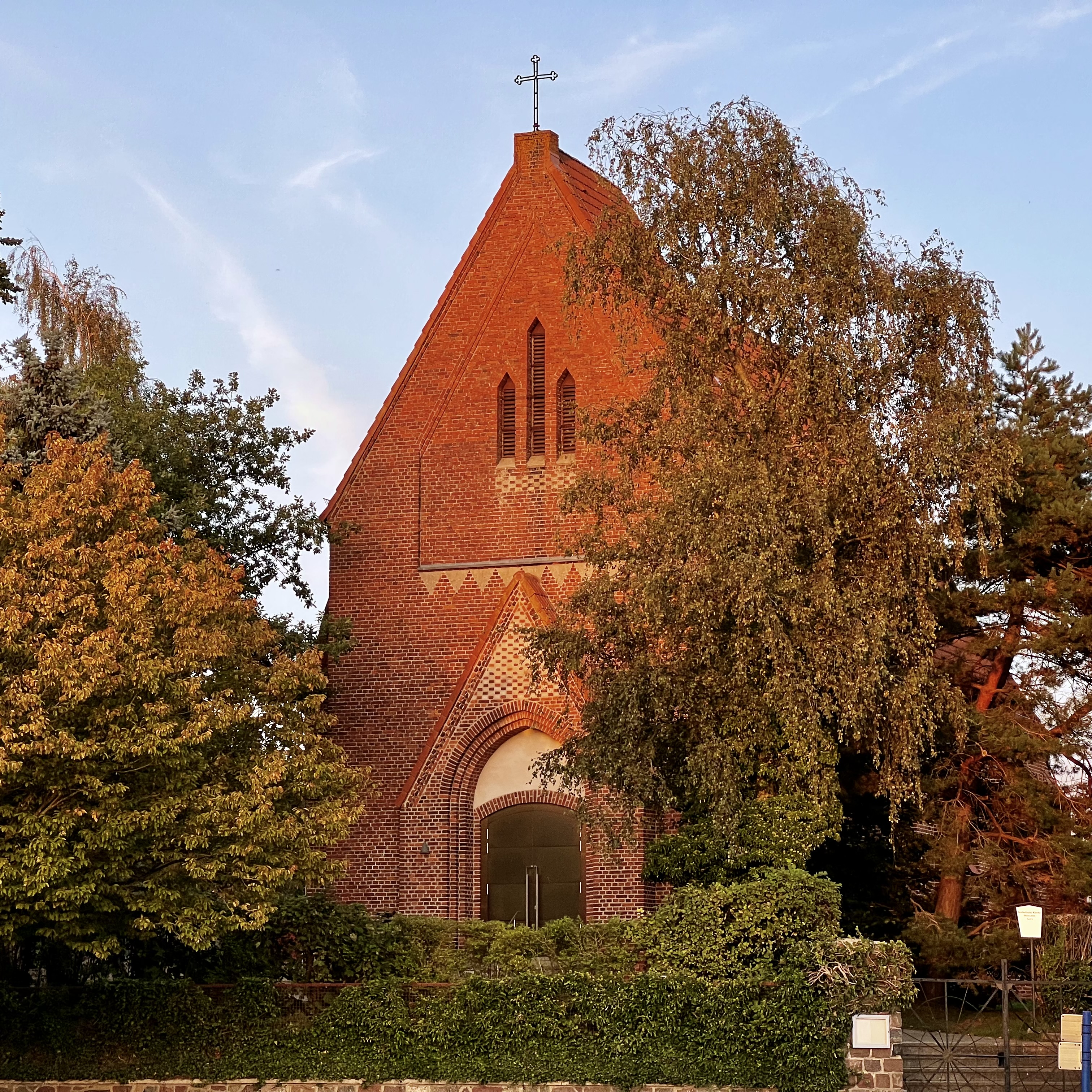 Backsteinkirche mit spitzem Dach und Kreuz.
