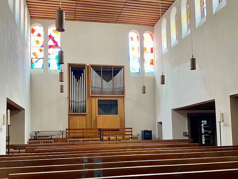 Kircheninnenraum mit Bänken, Orgel und Buntglasfenstern.