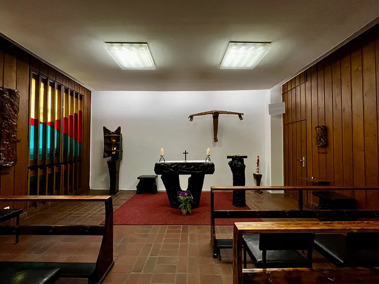 Kapelleninnenraum mit einem Altar und einem rustikalen Holzkreuz.