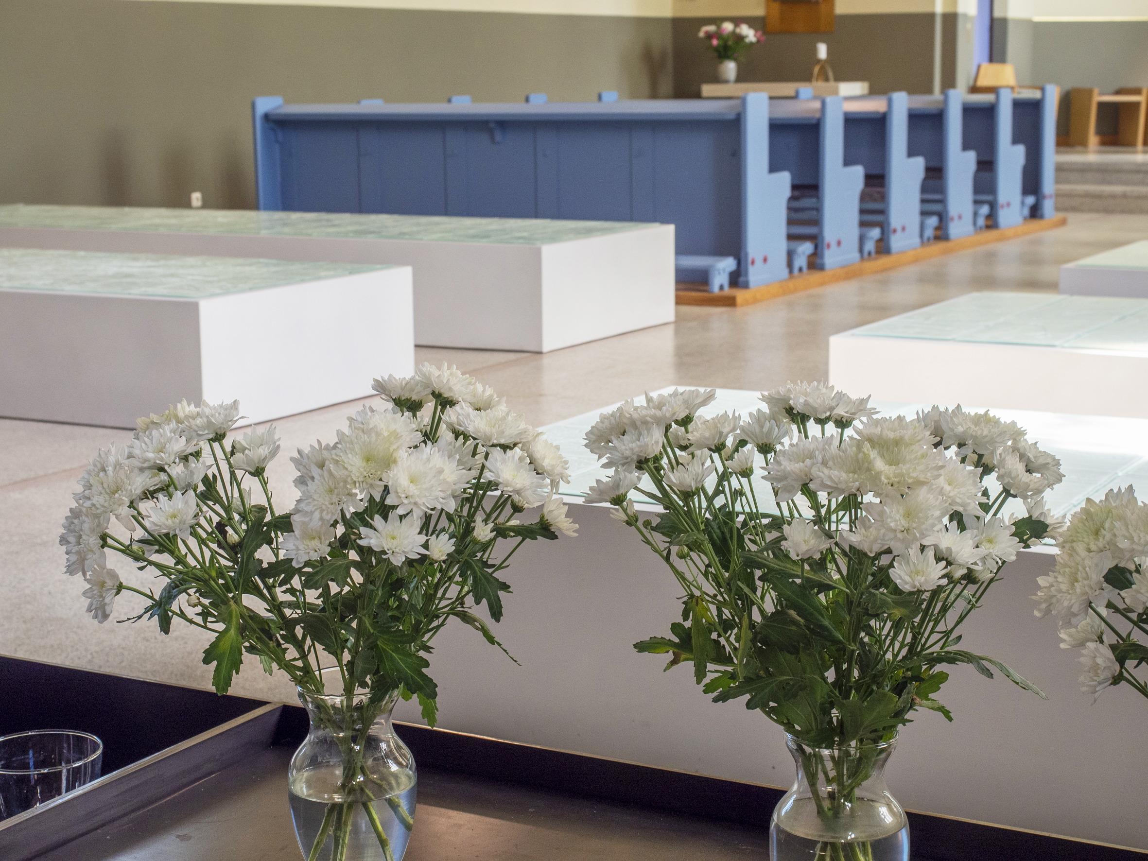 Weiße Blumen in Vasen im Vordergrund eines Kircheninnenraums.
