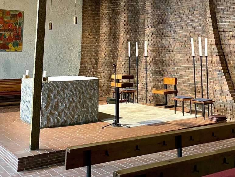 Kirchenraum mit einem Steinaltar und Backsteinwänden.