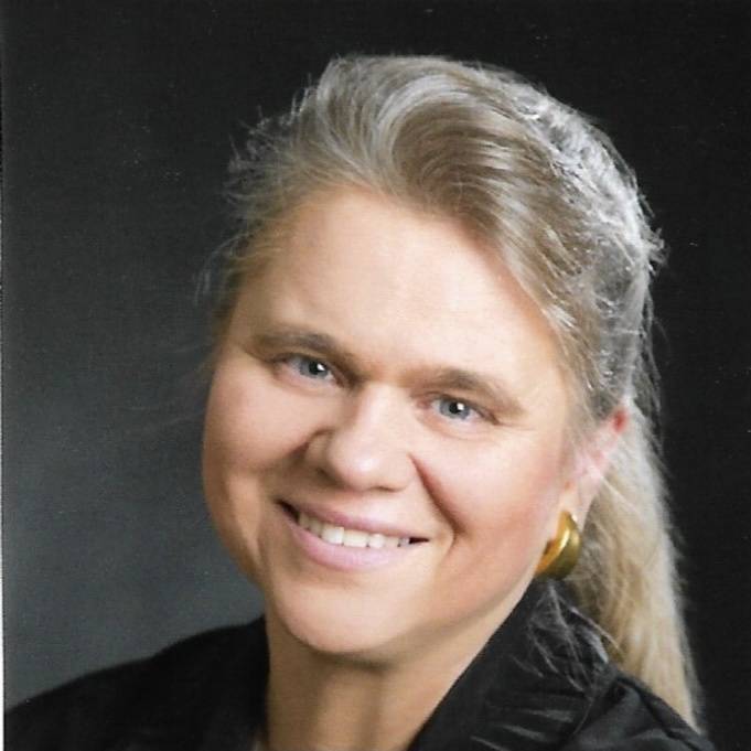 Porträt einer lächelnden Frau mit graumeliertem Haar und Zopf.